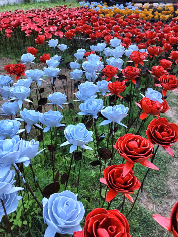 Rows of handcrafted red and blue fabric flowers with green stems arranged densely together on ground display