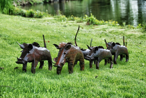 Group of dark bronze metal ostrich sculptures standing on green grass with water and trees in soft focus background