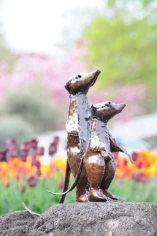 Bronze sculptural figurine of two stacked abstract forms on stone base with blurred garden flowers in background