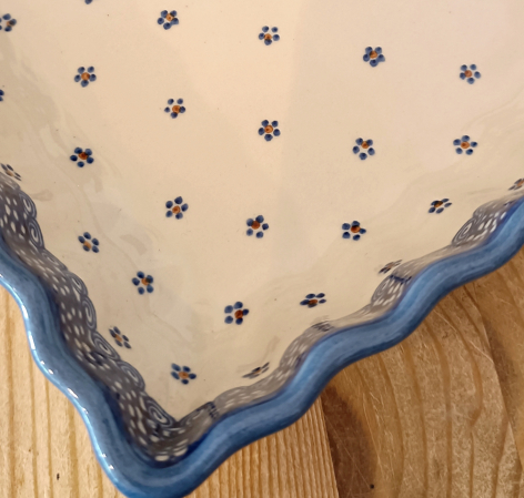 Beige textile with small indigo pattern details and blue embroidered scalloped border edge, flat lay view