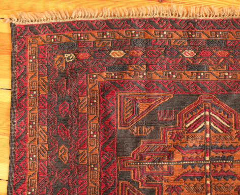 Deep red wool textile with ornate geometric patterns in gold and blue, traditional Afghan weaving