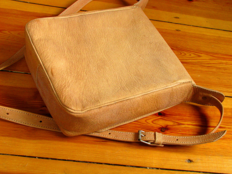 Tan leather shoulder bag with brown adjustable strap, displayed on wooden surface showing front and side view