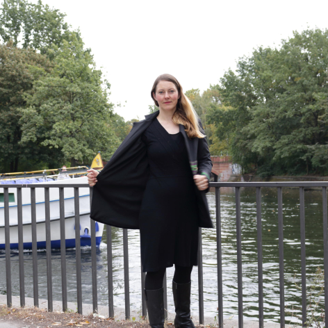 Woman wearing black leather jacket standing on bridge railing with trees and water in background