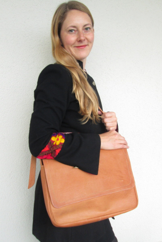 Woman wearing black blazer holding tan leather tote bag with red fabric accent detail, front view