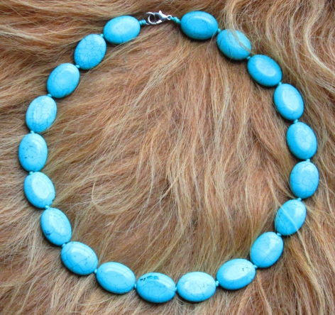 Bracelet de perles turquoise disposées en cercle sur fond texturé beige clair, vue de face