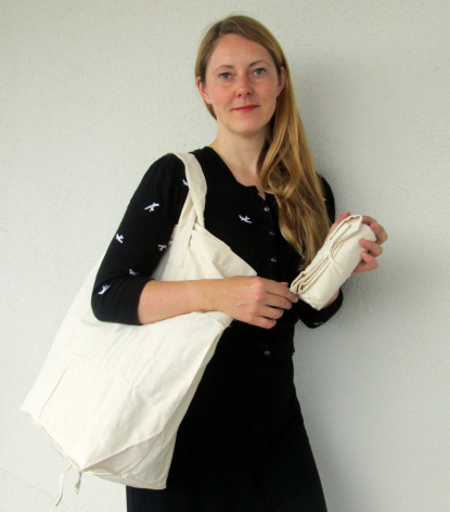 Woman in black dress holding cream leather shoulder bag with front view of structured tote design