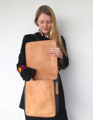 Woman wearing black blazer holding tan leather tote bag with structured rectangular panels, front view