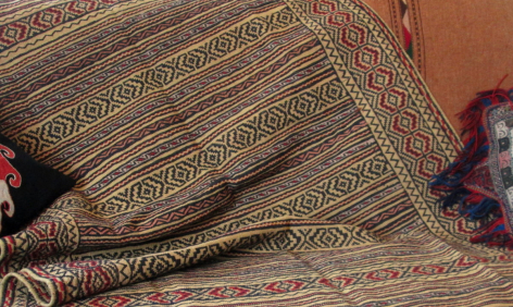 Détail de textile tissé aux motifs géométriques dorés et rouges, vue rapprochée des plis du tissu artisanal
