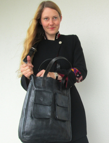 Frau trägt schwarze Ledertasche mit mehreren Taschen über der Schulter, Frontalansicht