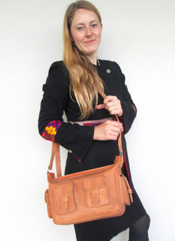 Frau trägt cognacfarbene Ledertasche mit Schultergurt über schwarzem Blazer, Frontalansicht