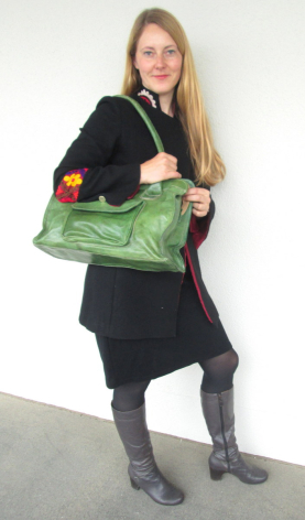 Woman holding a large green woven textile tote bag with colorful embroidered details, wearing black clothing