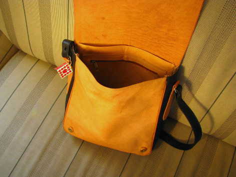 Sac à bandoulière en cuir orange vif ouvert montrant l'intérieur, avec anses noires, vue de dessus