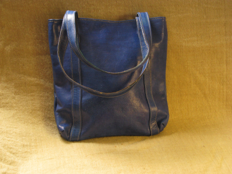 Deep blue leather tote bag with dual handles, front view, displayed on golden background