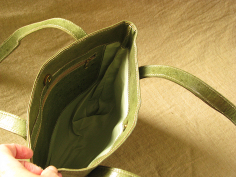 Open cream linen pouch with olive green interior lining, held in hand against wooden surface