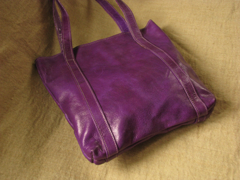 Purple leather shoulder bag with gathered sides on wooden surface, front view