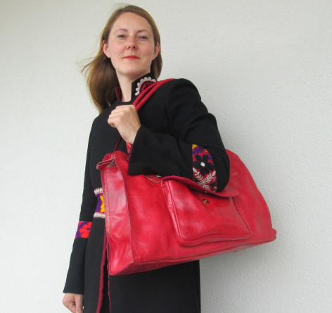 Sac à main rouge en cuir véritable avec détails noirs, porté sur l'épaule d'une femme vêtue de noir