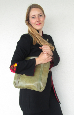 Frau trägt grüne Ledertasche mit Schulterriemen über schwarzer Jacke, Frontalansicht