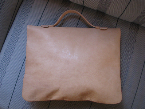 Tan leather tote bag with handles, front view, shown on wooden surface