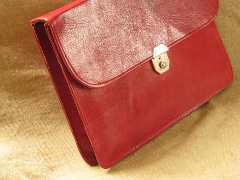 Red leather clutch bag with textured flap and silver toggle closure, front view angled on neutral background