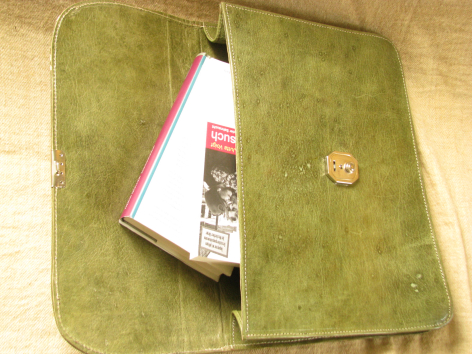 Green suede clutch wallet open with magazine inside, front view showing snap closure detail