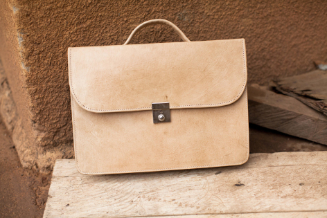 Serviette en cuir beige vue de face avec fermoir métallique et poignée, posée sur une surface rustique
