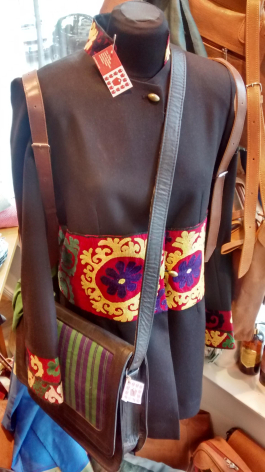Dark brown leather jacket with colorful embroidered patches on chest, displayed on hanger with price tag visible