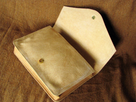 Tan leather clutch wallet open to show interior compartments, viewed from above on wooden surface