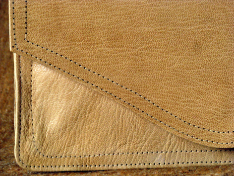 Sac en cuir beige clair avec détail de couture pointillée et coin replié montrant la doublure intérieure