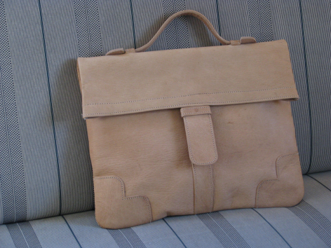 Tan leather satchel with flap closure and structured compartments, front view against wooden background