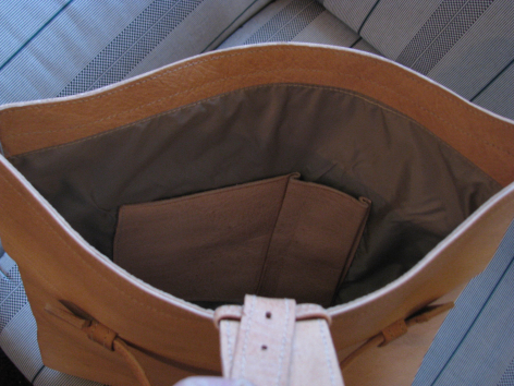 Tan leather tote bag shown open from above, revealing dark brown interior lining with white price tag attached to rim