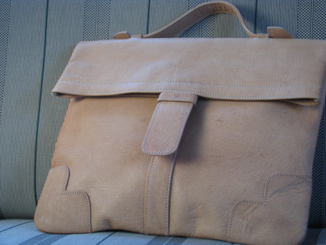 Tan leather messenger bag with flap closure and shoulder strap, front view showing worn patina finish