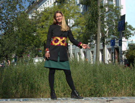 Woman in black outfit holding yellow sunflowers standing outdoors among green trees and foliage