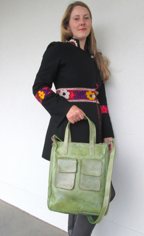 Woman wearing black jacket with pink belt holding green canvas tote bag with multiple pockets, front view