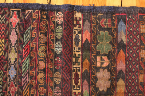 Folded textile fabrics in rich jewel tones displaying intricate geometric and figurative patterns stacked in rows