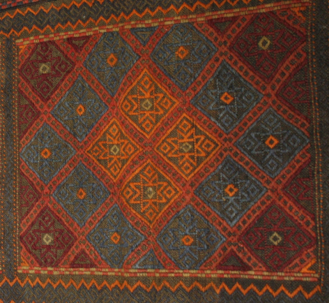 Rust red textile with teal and gold diamond pattern, flat lay view showing traditional woven design and border detail