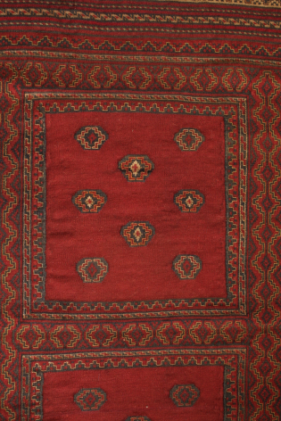 Red textile with geometric diamond patterns and ornamental border in earth tones, flat lay view