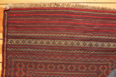 Red and burgundy woven textile with geometric striped patterns and gold-toned border, flat lay detail view