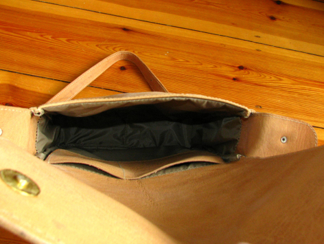 Black leather pouch with natural tan trim, open view showing interior compartment, displayed on wooden surface