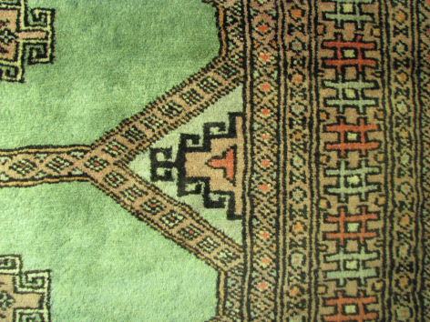 Green textile with geometric patterned border and decorative trim detail, flat lay view