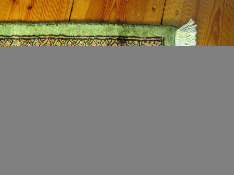 Woven textile trim with green geometric pattern on natural fiber band, displayed on wooden surface