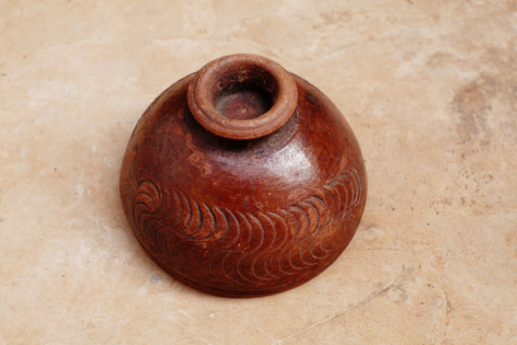 Terracotta clay pot with rounded bulbous body and narrow opening, viewed from above on neutral surface