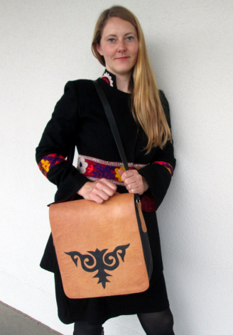Frau trägt karamelfarbene Ledertasche mit schwarzem geometrischem Muster auf der Vorderseite über der Schulter