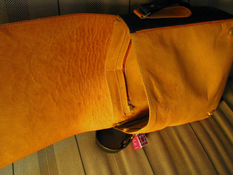 Tan leather bag viewed from above showing curved body and black handles with pink detail accent