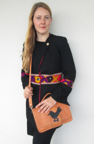 Woman wearing black blazer and patterned belt holding tan leather crossbody bag, front view