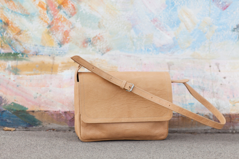 Hellbraune Ledertasche mit Schultergurt, Vorderansicht, auf strukturiertem Hintergrund mit Kunstwerk