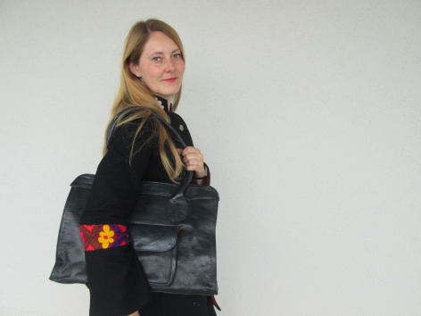 Femme portant un sac à main en cuir noir de forme carrée avec détails ornementaux rouges et dorés, vue de trois quarts