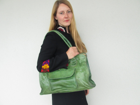 Woman wearing black clothing holding a large green fabric tote bag with colorful embroidered details on the front