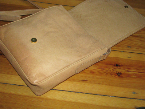Beige Ledertasche mit rundem Verschluss liegt auf Holzoberfläche, Draufsicht
