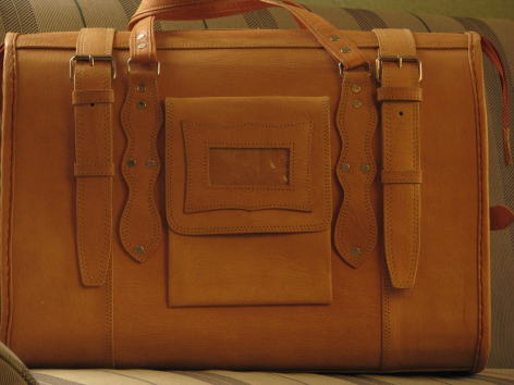 Tan leather tote bag with dual handles and front pocket, viewed from front angle