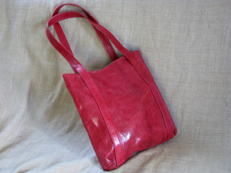 Hot pink leather tote bag with dual handles, displayed flat on white fabric background